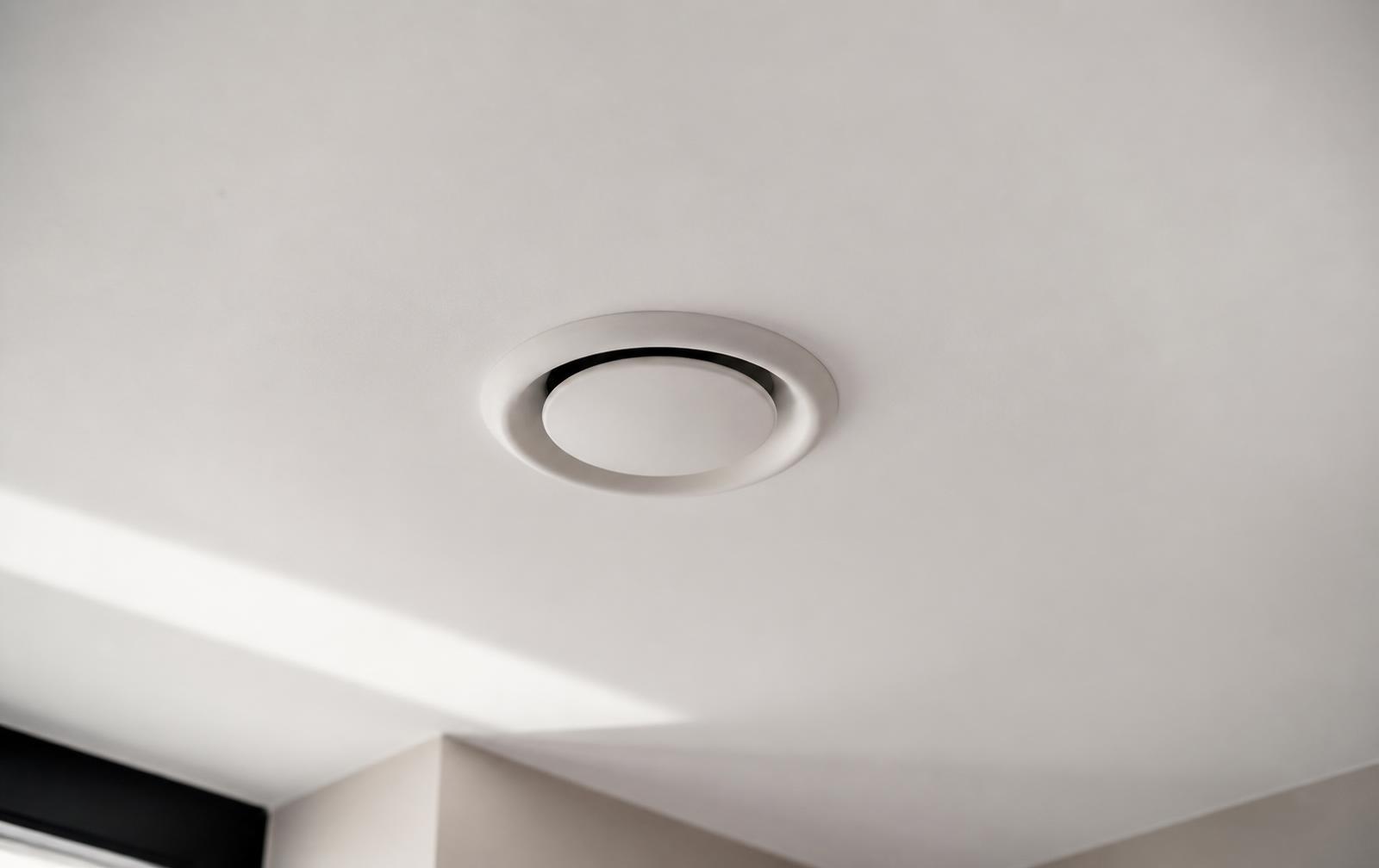 Wit ventilatieventiel in het plafond van een moderne woning, met zacht daglicht
